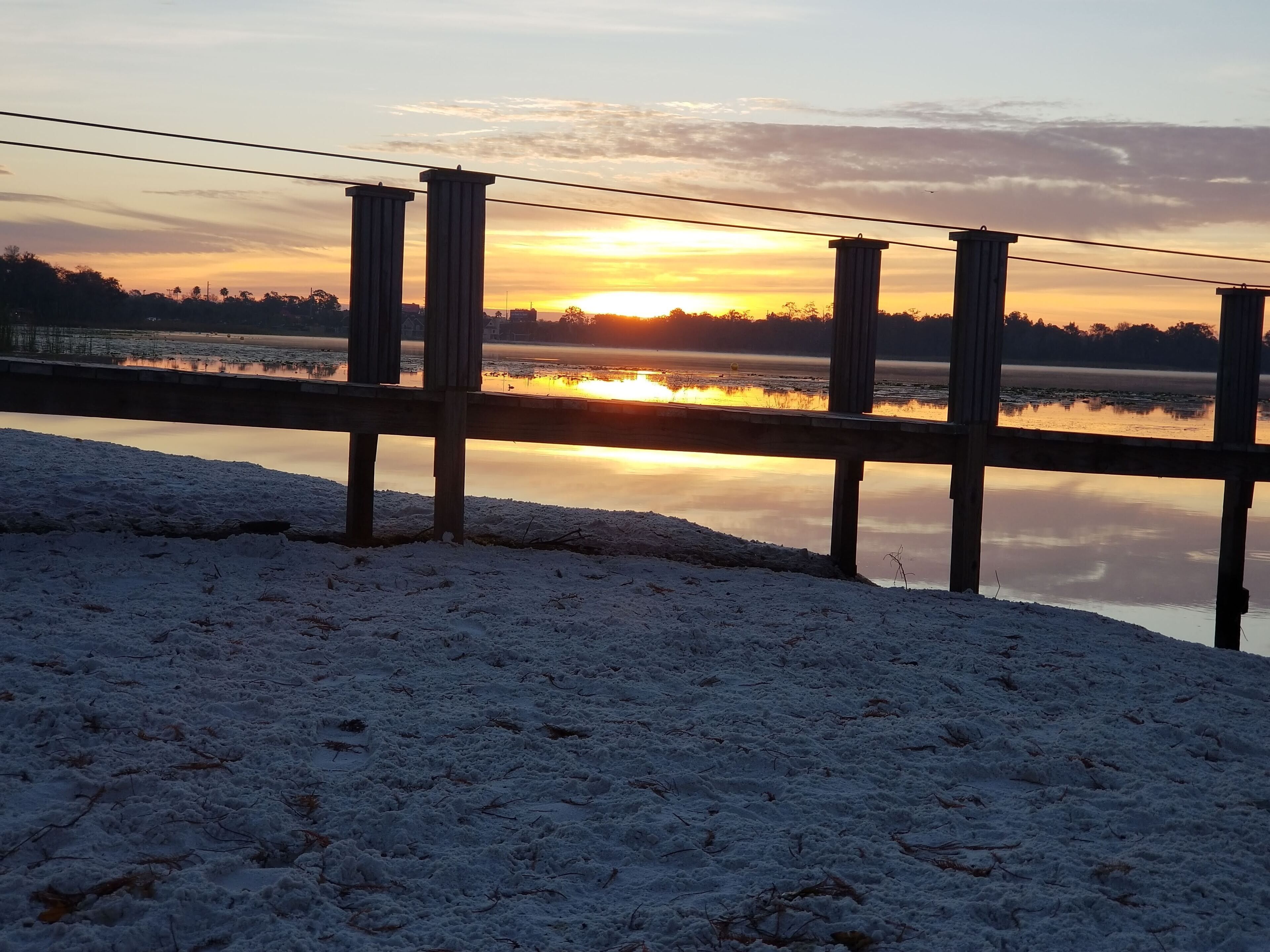 A wooden pier extending over a frozen lake with a sunset in the background.