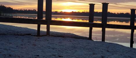 A wooden pier extending over a frozen lake with a sunset in the background.