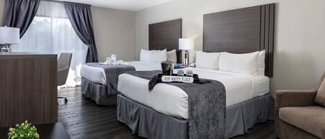 A hotel room with two beds, a desk, a chair, a lamp, and a small plant.