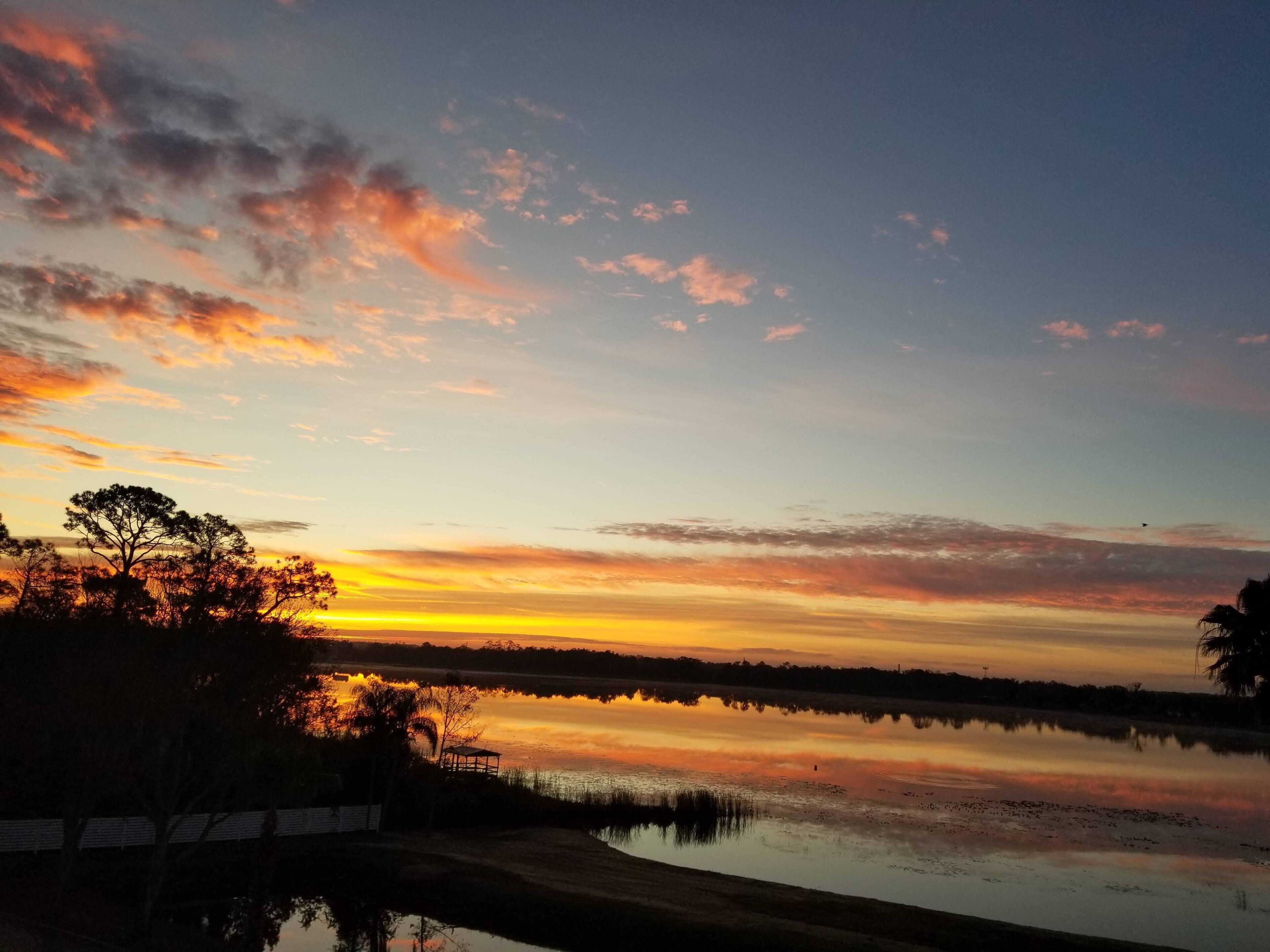 Un atardecer sobre un lago tranquilo, con siluetas de árboles contra el cielo.