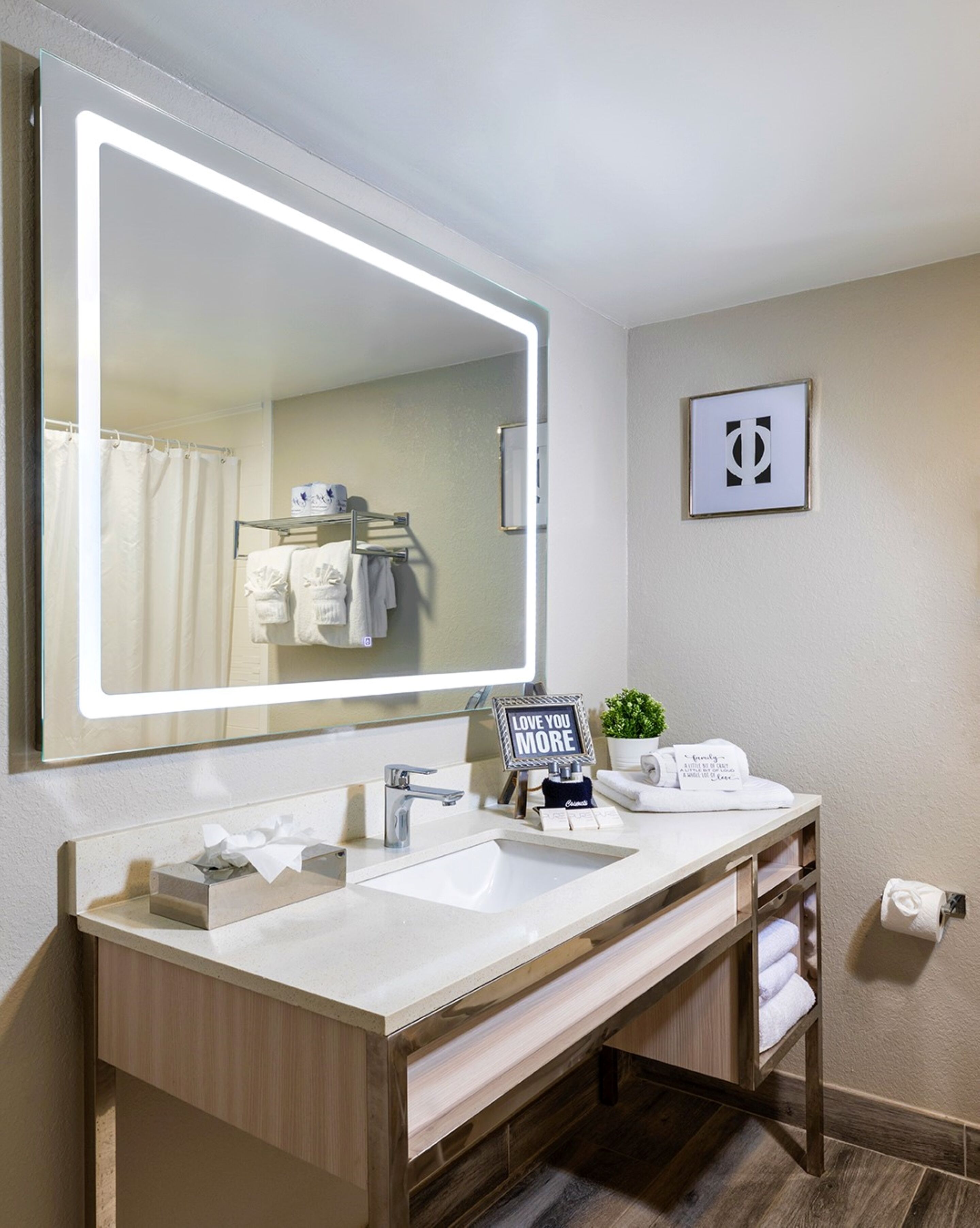 A modern bathroom with a large mirror, two sinks, a towel rack, and a framed picture on the wall.