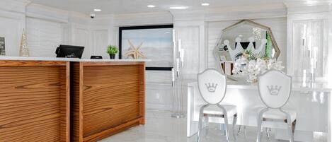 A reception area with a wooden reception desk, two white chairs with crown designs, a large mirror, and a starfish decoration.