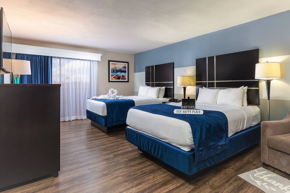 A hotel room with two beds, a desk, a chair, and a view of the outdoors.