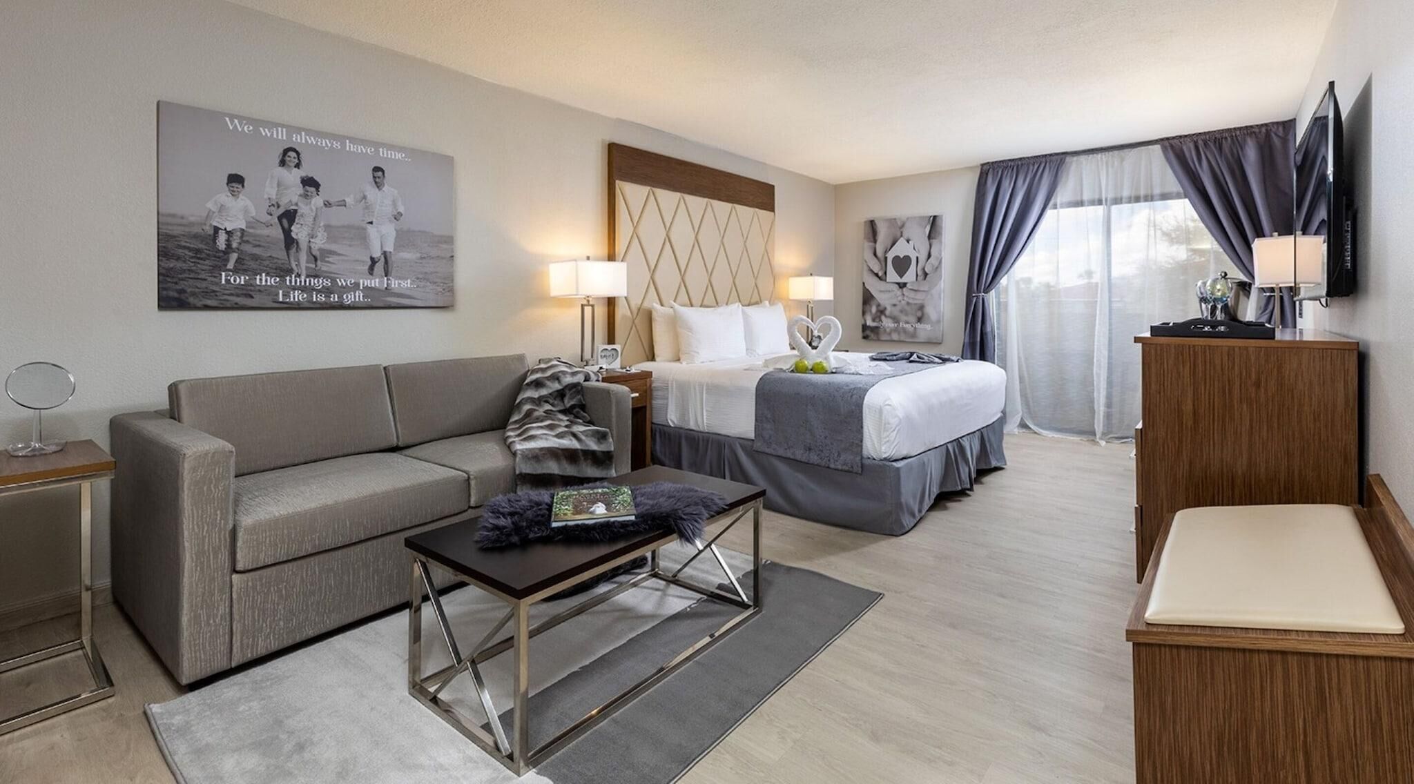 Une chambre d’hôtel avec un lit, un canapé, une table basse, une télévision et une affiche au mur.