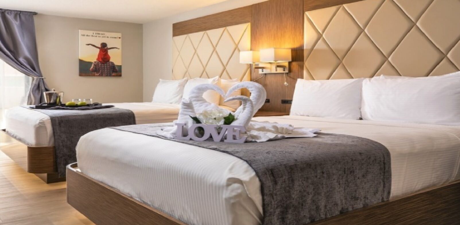 Une chambre d’hôtel avec deux lits, un mur décoratif orné d’un motif géométrique, une lampe fixée au mur et un tableau encadré.