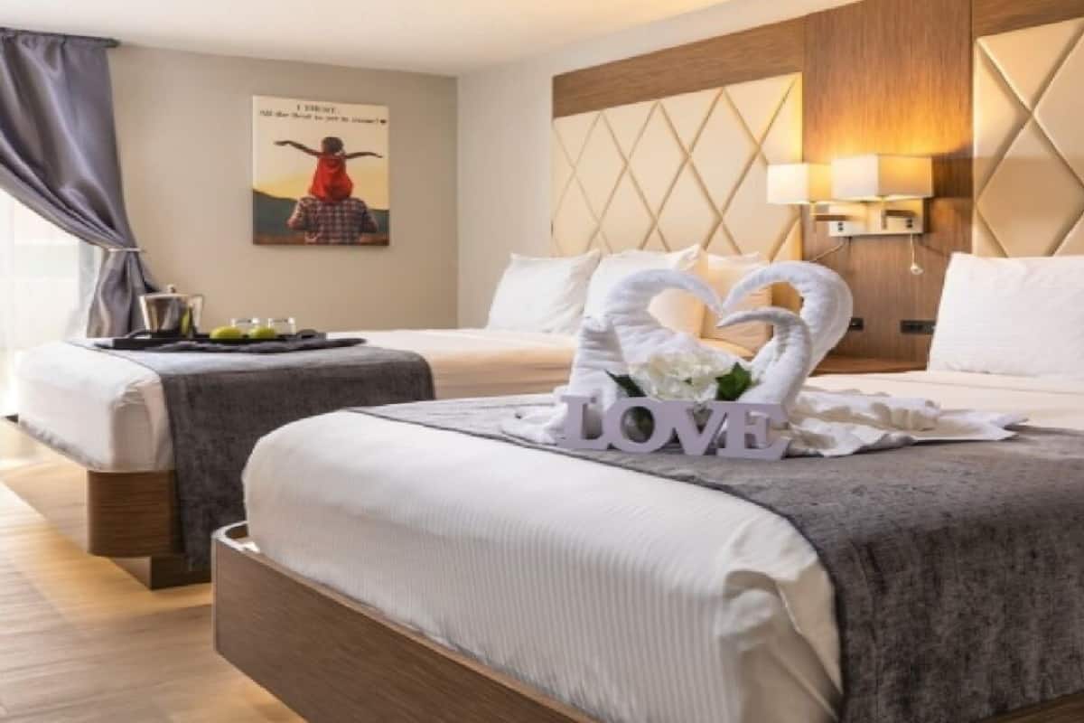 Hotellihuone, jossa on kaksi sänkyä, koristeellinen seinä, jossa on geometrinen kuvio, seinään kiinnitetty valaisin ja kehystetty taulu.