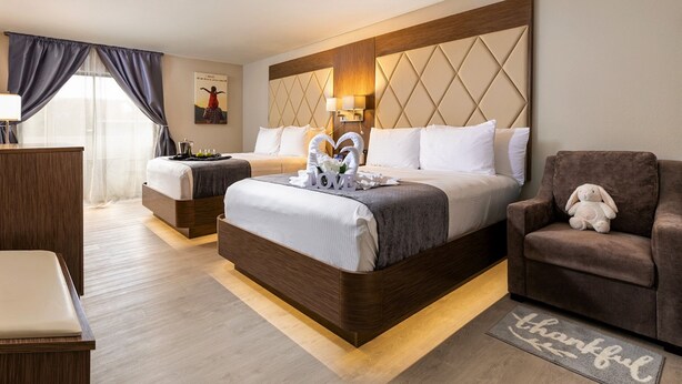 A hotel room with a large bed, a smaller bed, a desk, and a chair. There is a decorative item on the bed and a rug on the floor. - Palazzo Lakeside Hotel (Kissimmee)