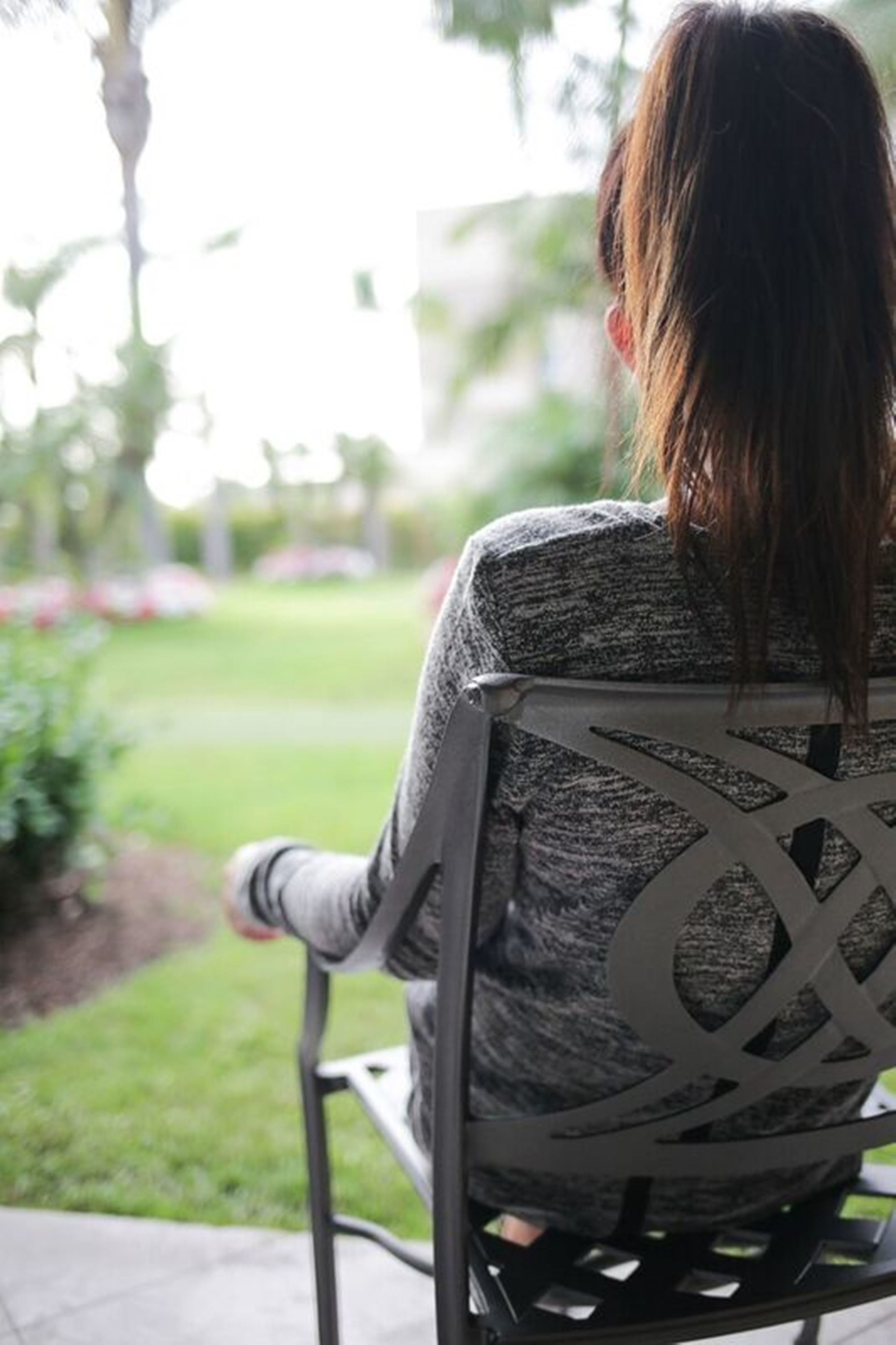 A person sitting on a chair with a geometric backrest design, outdoors with a view of a garden and a pathway.