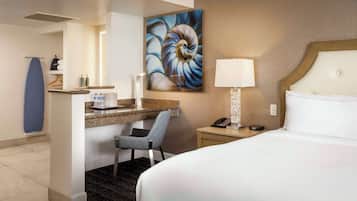 Habitación de hotel con una cama, un escritorio y una silla, una mesita de noche, una lámpara de pared y un cuadro abstracto grande.