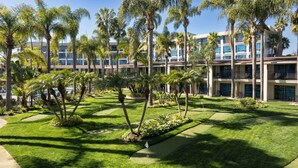 Un hôtel doté d’une pelouse bien entretenue, de palmiers et d’un espace piscine.