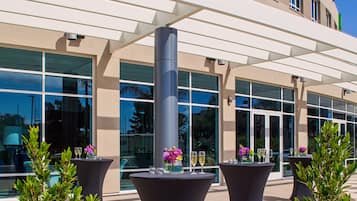 A modern building with large windows and outdoor seating areas with tables and chairs.
