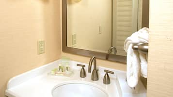Un baño con lavamanos blanco, dos grifos, un espejo y un perchero para toallas.