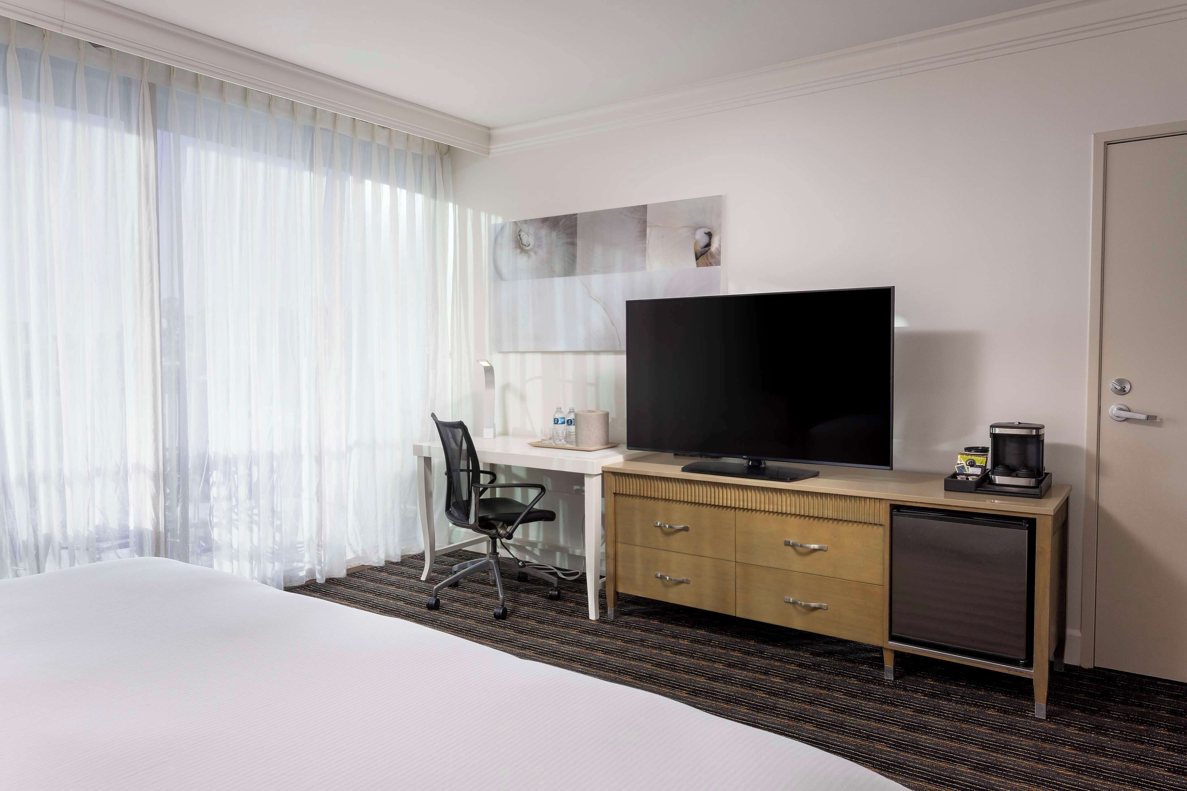 A hotel room with a bed, a desk with a television, a chair, a coffee maker, and a wardrobe.