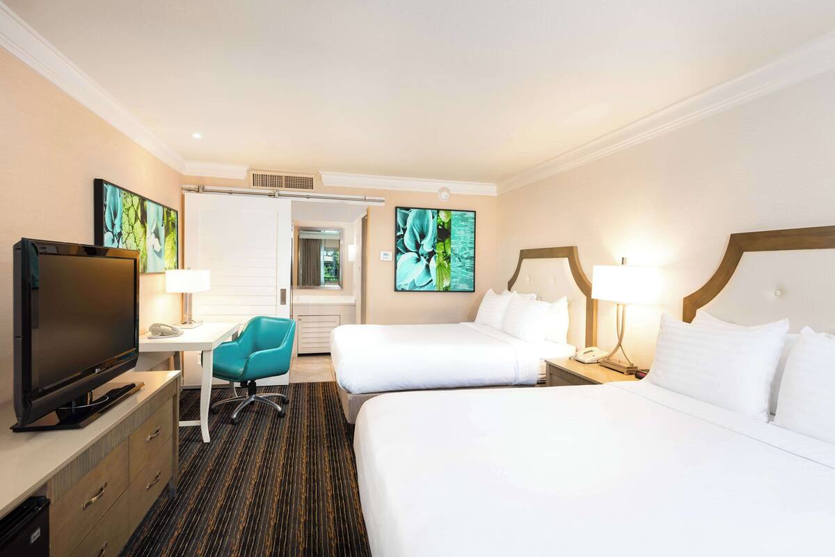 A hotel room with two beds, a desk with a television, a chair, and artwork on the walls.