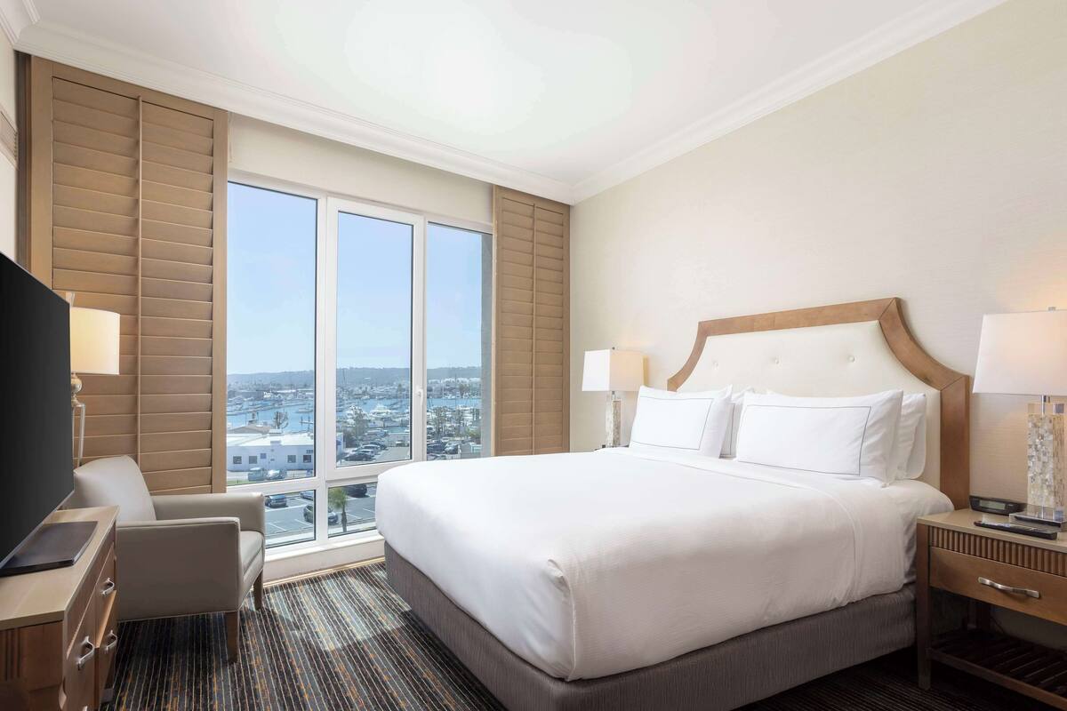 A hotel room with a large bed, a desk, a chair, and a TV.