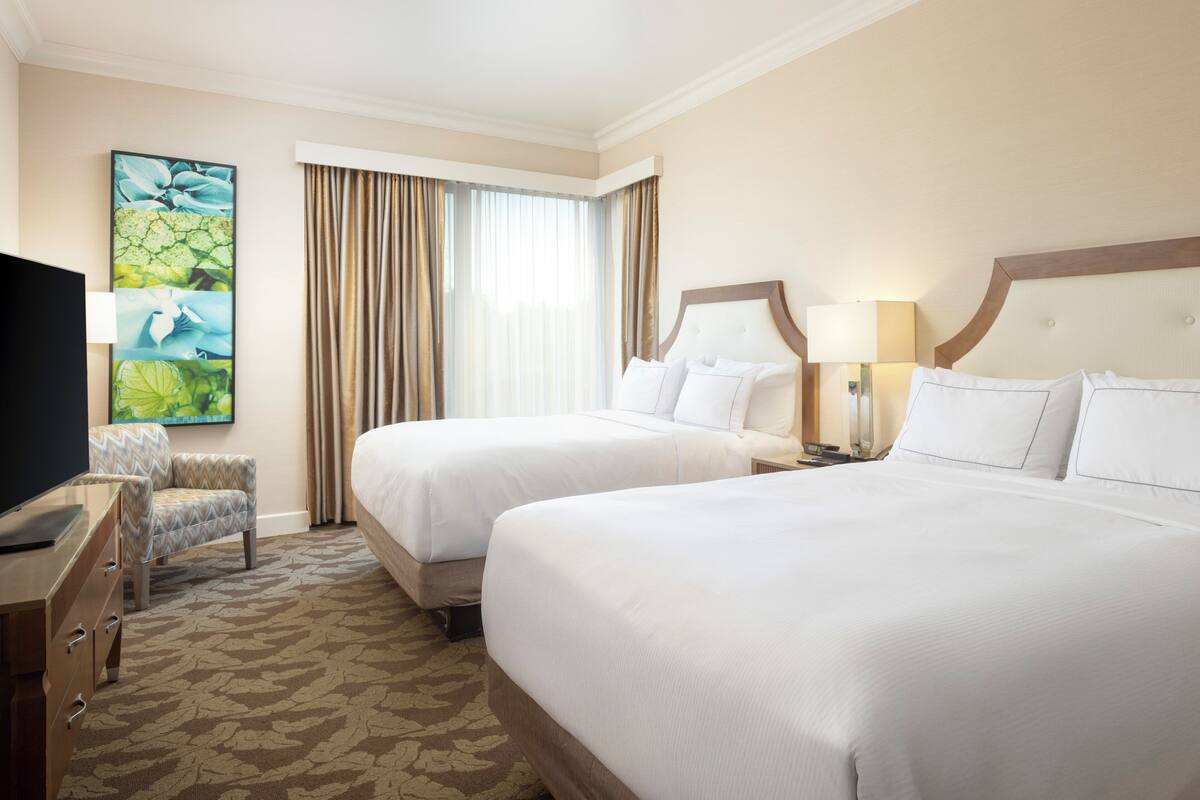 A hotel room with two beds, a TV, a desk, and a chair.