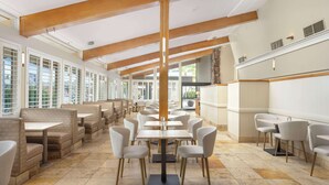 Un vaste espace de restauration intérieur doté de hauts plafonds, de poutres en bois et d’un mélange de banquettes et de tables.