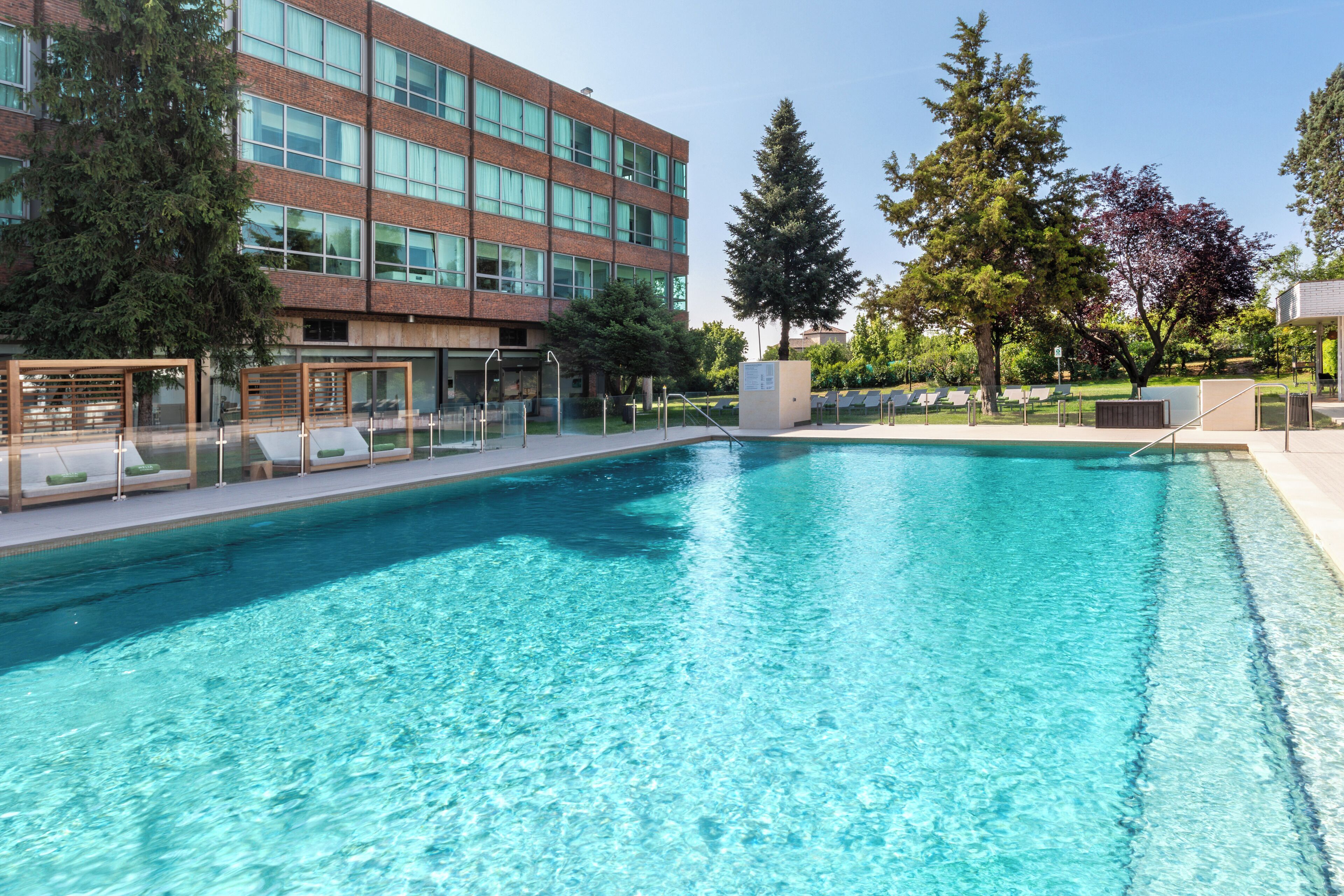 A clear swimming pool with lounge chairs and a modern building in the background.