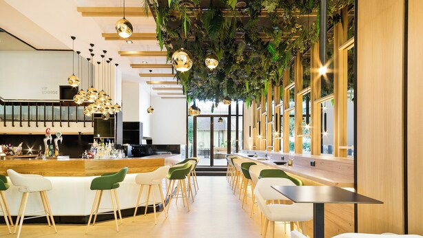 Un área de bar moderna con una barra alargada, varios taburetes y lámparas colgantes.