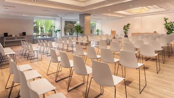 A conference room with rows of white chairs and tables, large windows with a view of trees, and a chandelier.