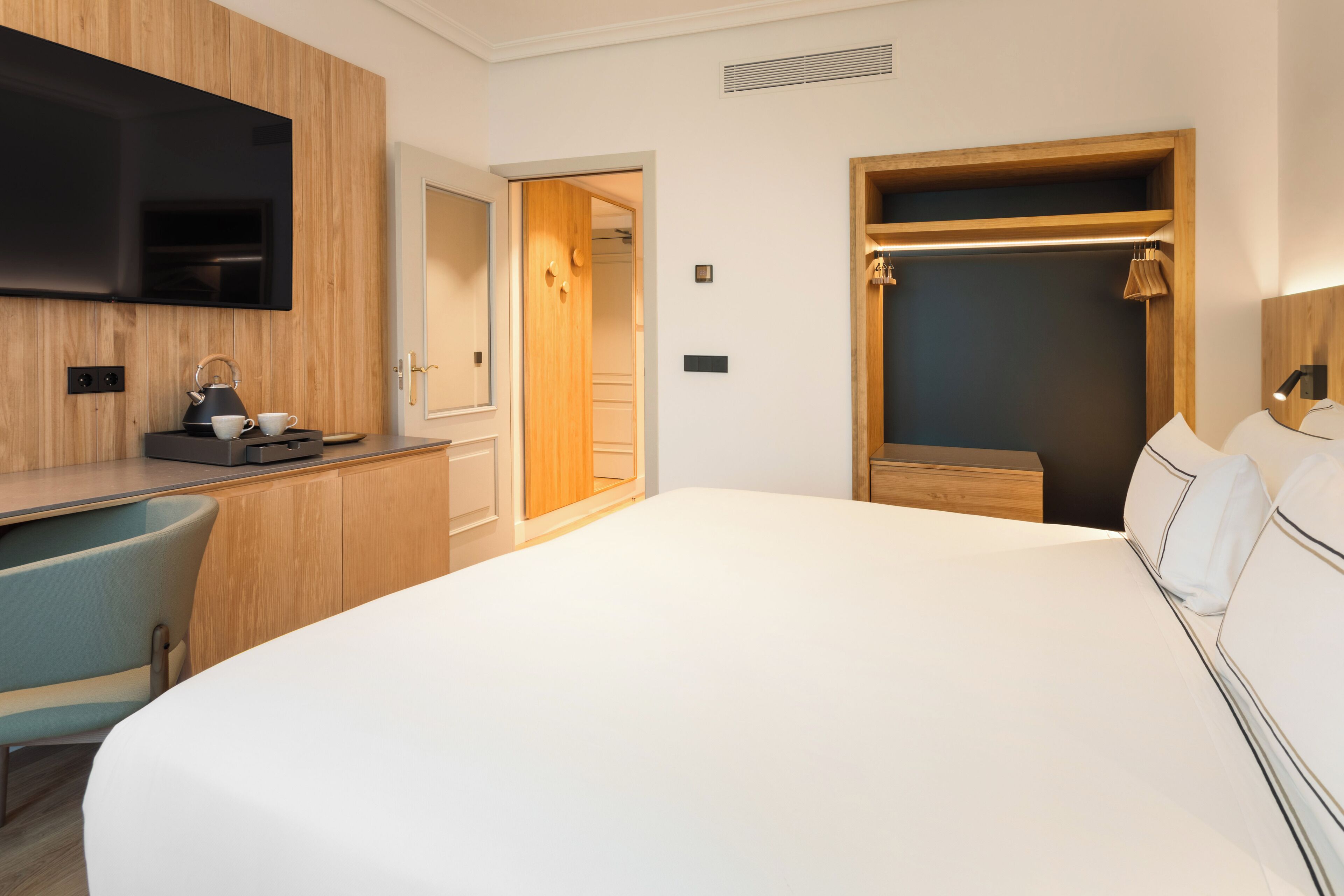 Habitación de hotel con una cama grande, un escritorio con hervidor, televisión y armario.