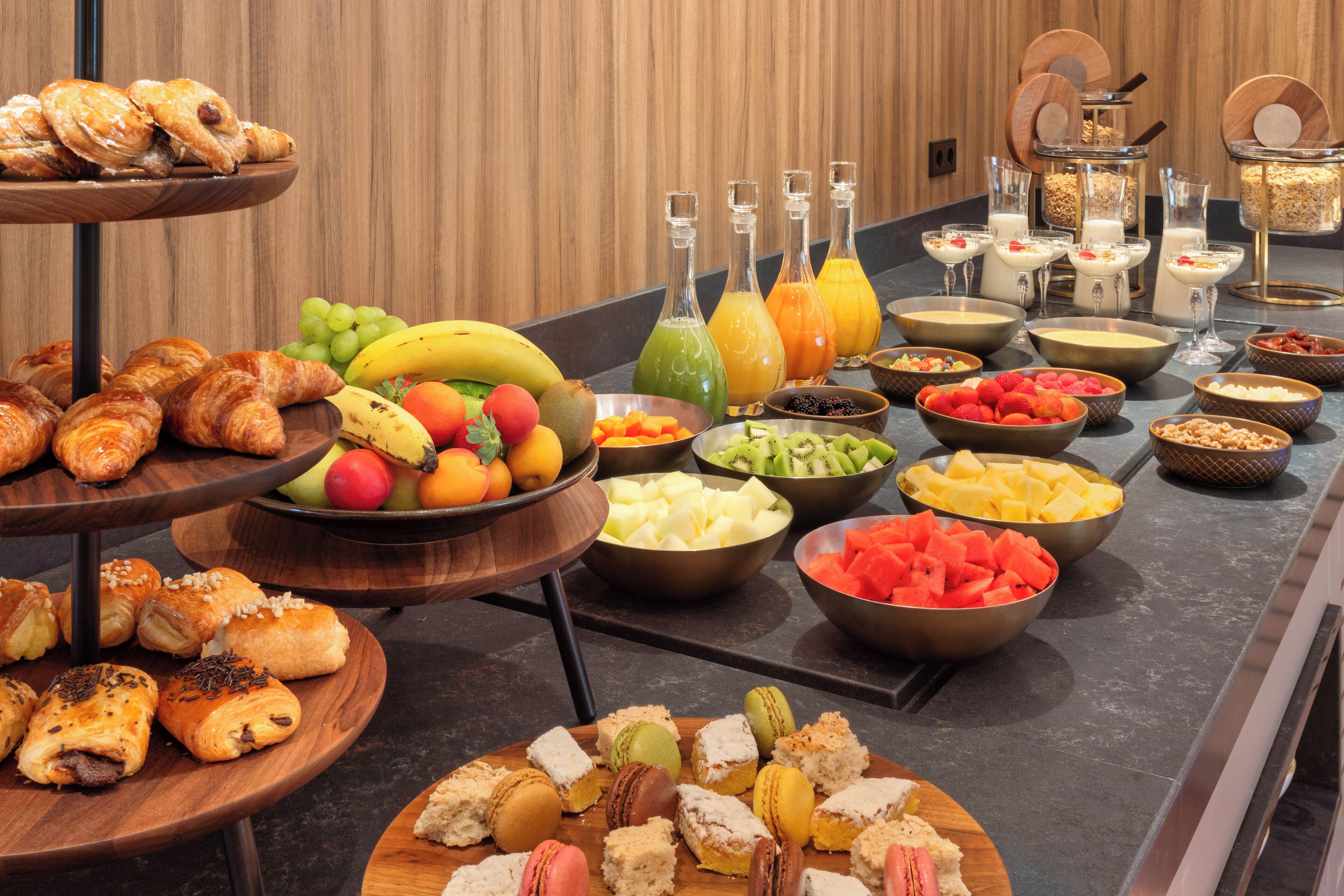 Un bufé con distintos alimentos, como pasteles, frutas y bebidas.