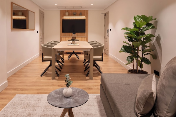 A modern dining area with a wooden table and chairs, a large mirror, a flat-screen TV, and a potted plant.