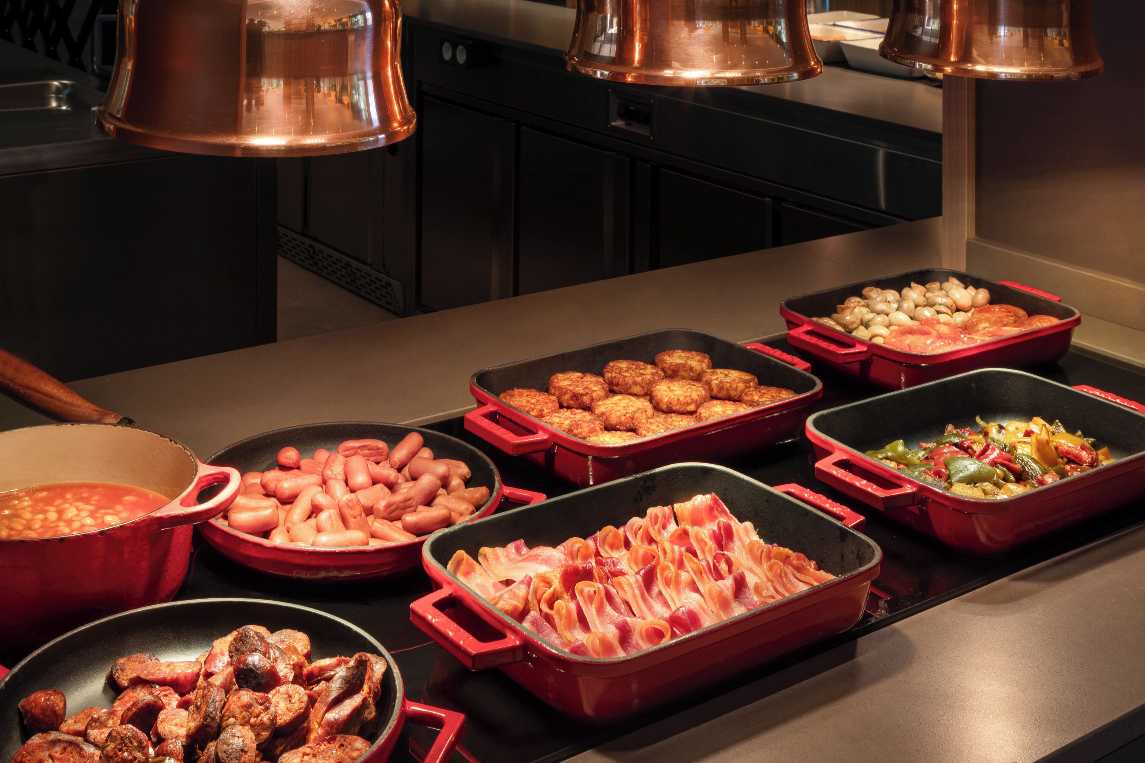 Un buffet proposant divers plats, notamment des saucisses, des haricots et des légumes.