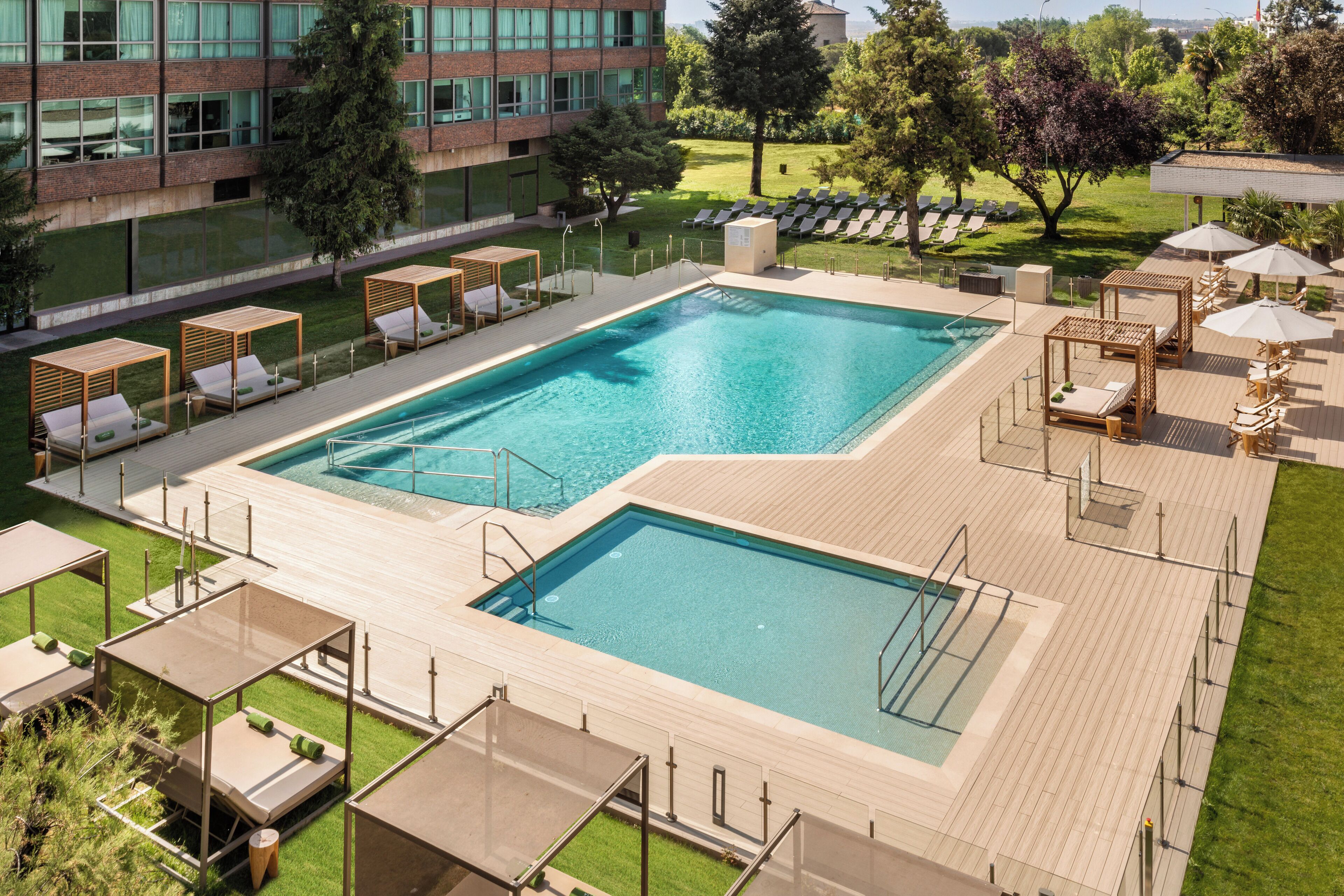 Zona de piscina con sillones de descanso, terraza de madera y vista a un edificio al fondo.