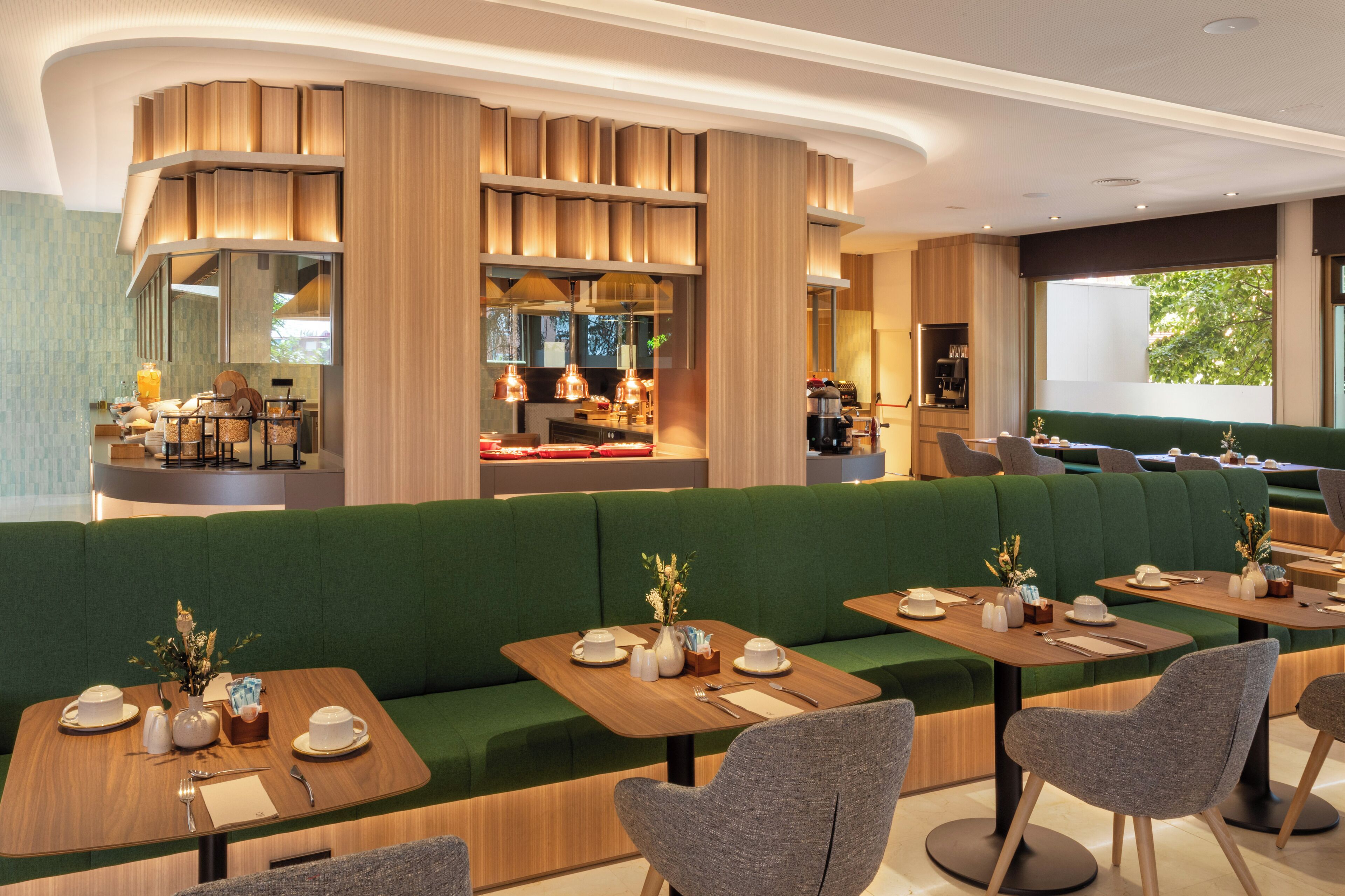 A modern restaurant with green upholstered seating, wooden tables, and ambient lighting.
