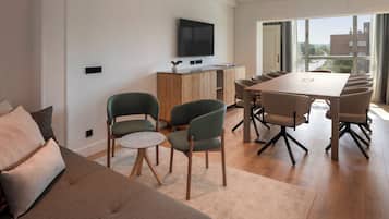 Una sala de estar moderna con un sofá, sillas, una mesa de comedor y un televisor montado en la pared.