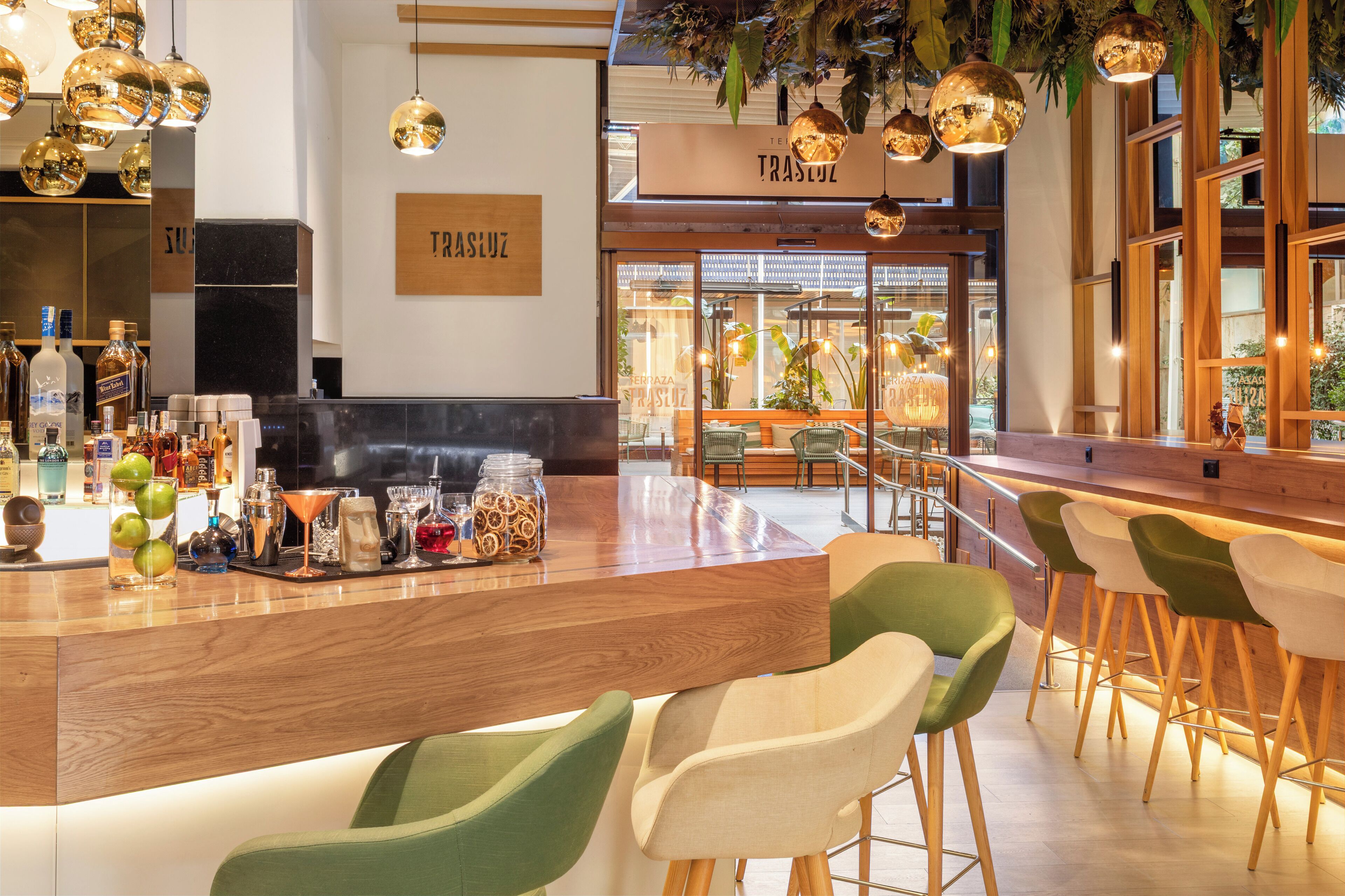 A bar area with a wooden counter, green and white chairs, hanging spherical lights, and a sign reading 'TRASULZ'.