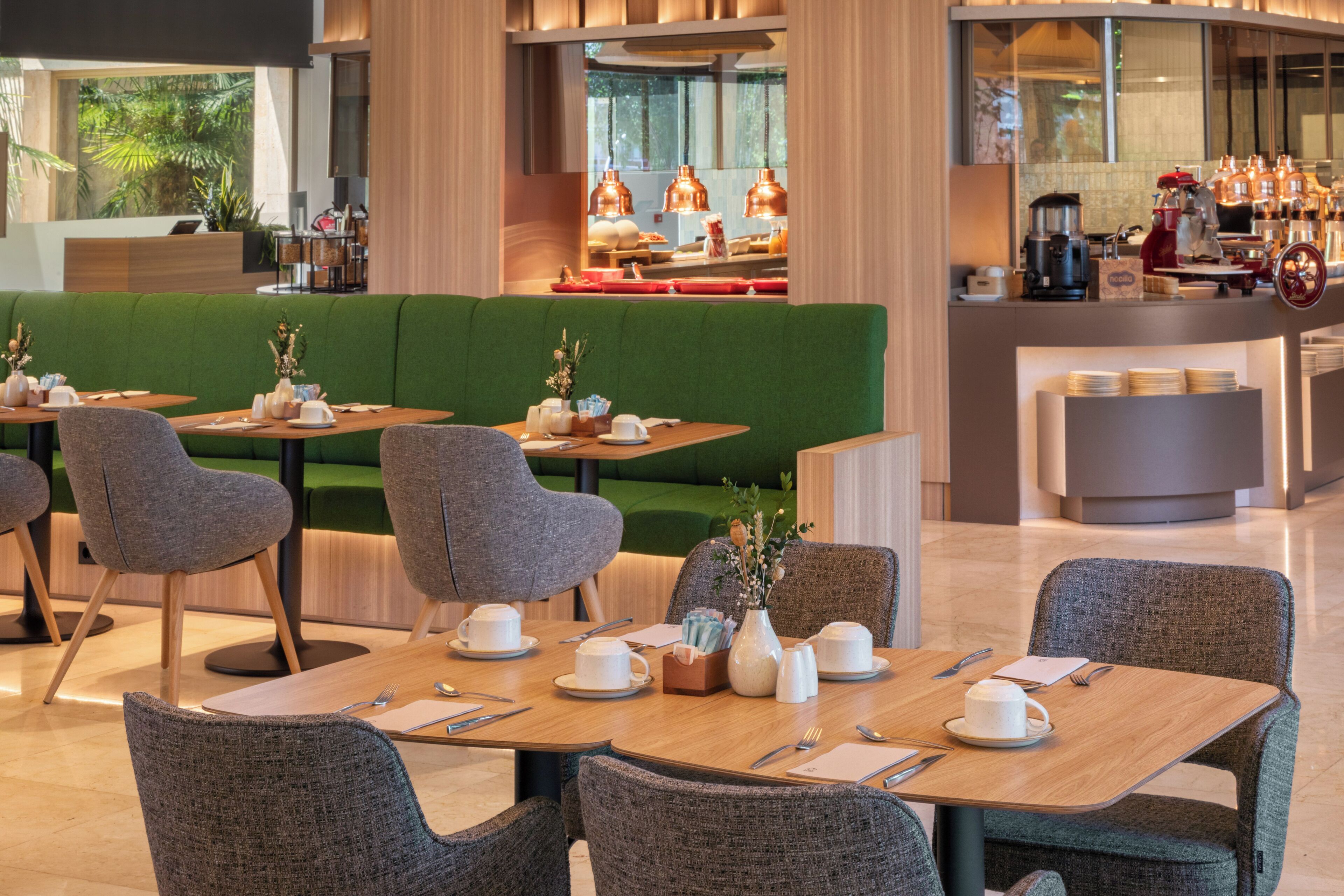 Un comedor moderno con asientos verdes, mesas de madera y una barra de café al fondo.