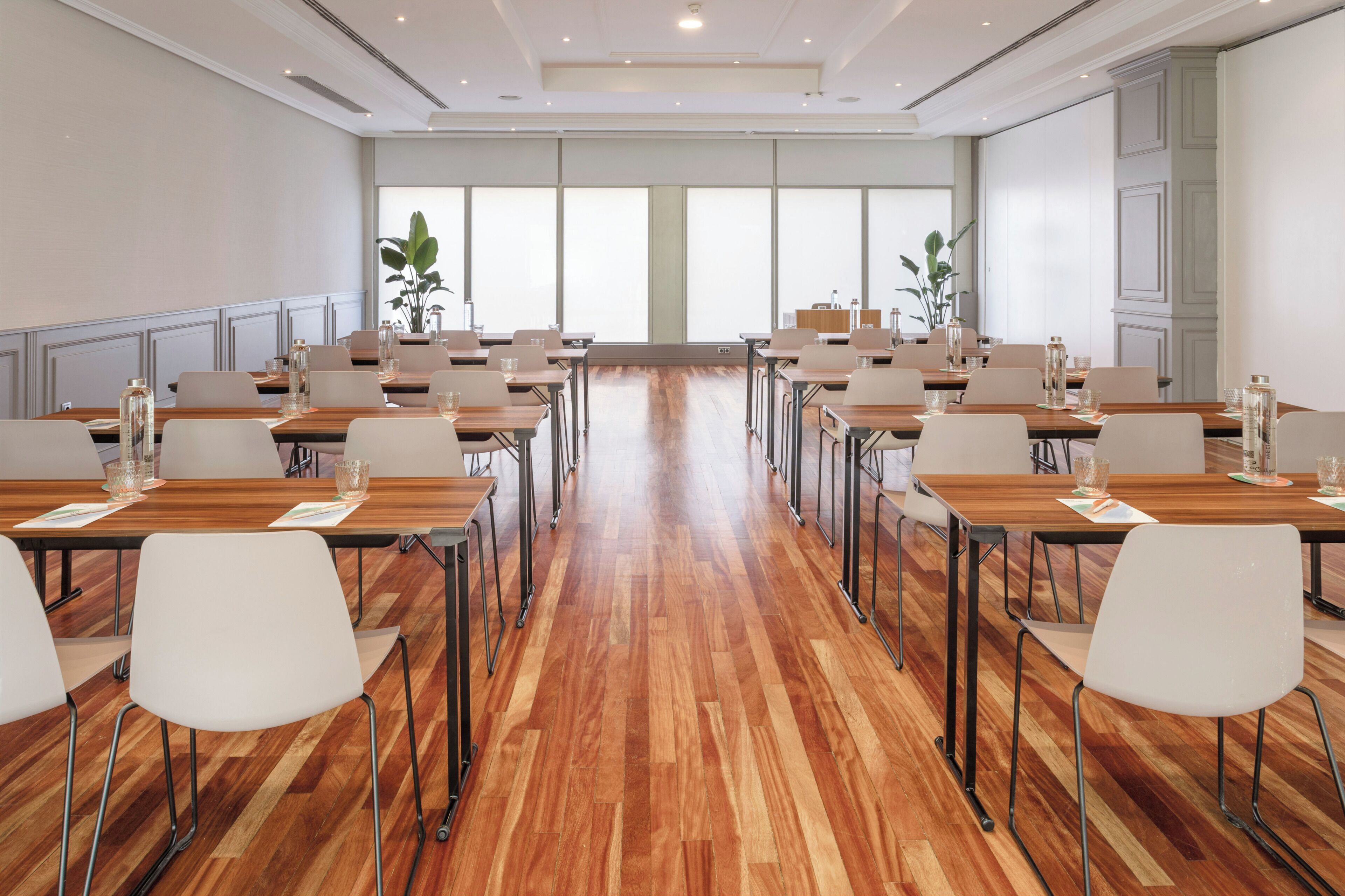 Un salón de conferencias con varias mesas y sillas, ventanas amplias y suelo de madera.