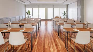 Un salón de conferencias con varias mesas y sillas, ventanas amplias y suelo de madera.