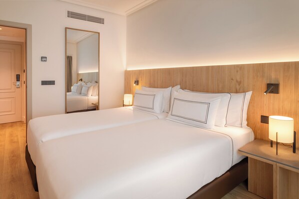 A large bed with white linens, a wooden headboard, bedside lamps, and a mirror.