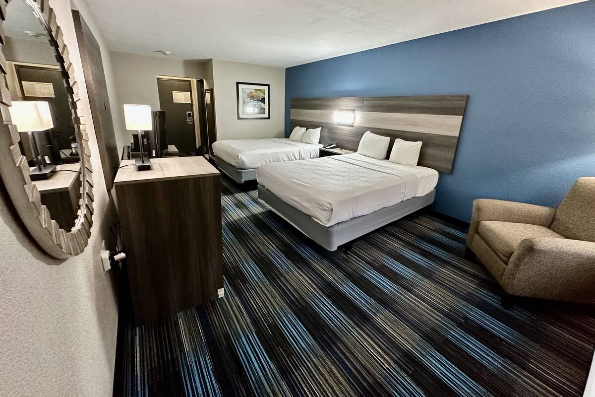Habitación de hotel con dos camas, un escritorio, una silla y un espejo grande.