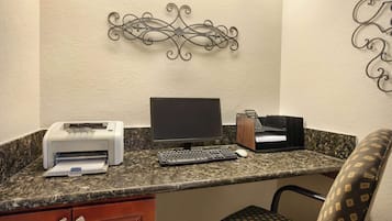 A small office area with a desktop computer, a printer, and a keyboard on a granite countertop.
