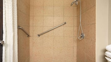 En duschhörna med beige kakel, ett stödhandtag och ett duschmunstycke som kan hållas i handen.