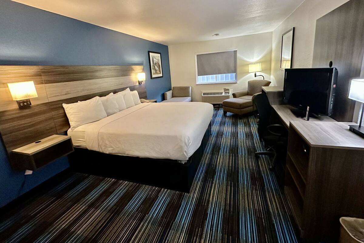 Una habitación de hotel con una cama grande, mesitas de noche, un escritorio, una silla, un televisor y una ventana con persianas.
