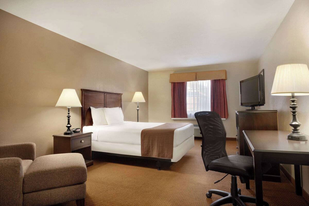 Una habitación de hotel con una cama, mesitas de noche con lámparas, un escritorio con una silla, un televisor y una ventana con cortinas.