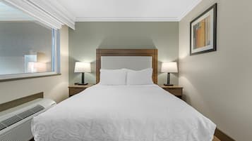 A neatly made bed with a white bedspread, two bedside lamps, a framed picture on the wall, and a window with a view of the outside.