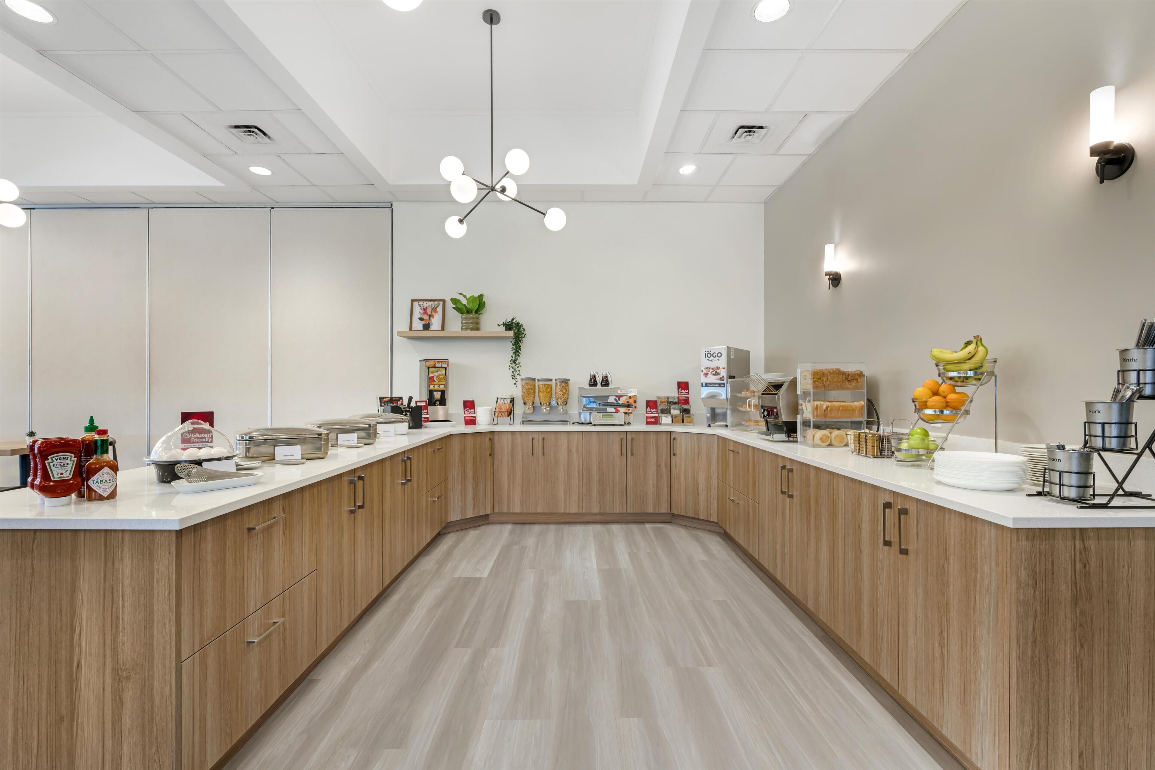 A modern kitchen with a curved counter, wooden cabinets, and various food items and kitchen appliances.