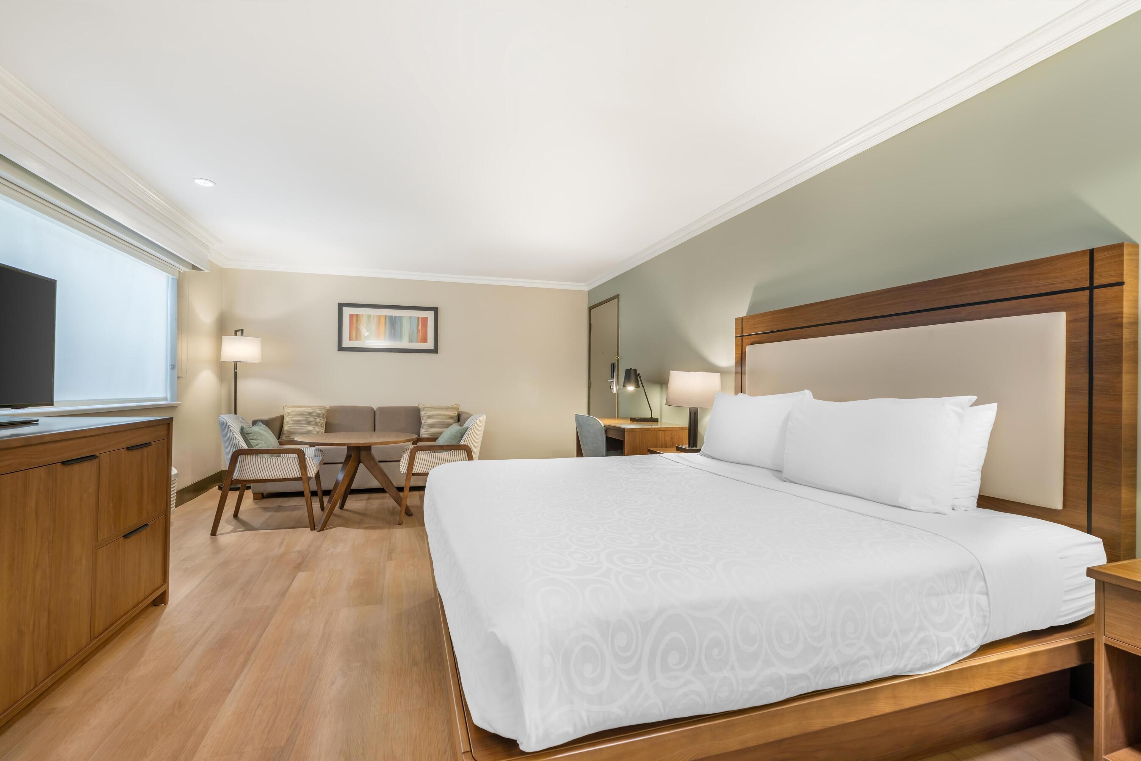 A hotel room with a large bed, a desk, a chair, a TV, and a painting on the wall.