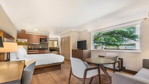 Una habitación de hotel moderna con cama, zona de comedor, cocina y televisor.