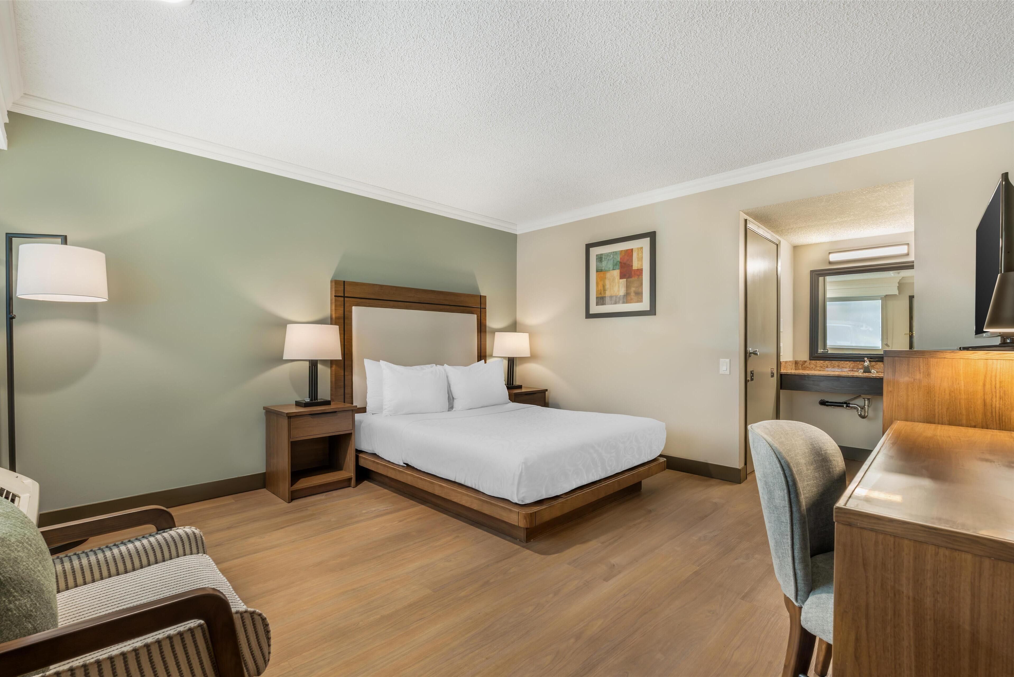 A hotel room with a bed, bedside tables, a desk, a chair, and a mirror.