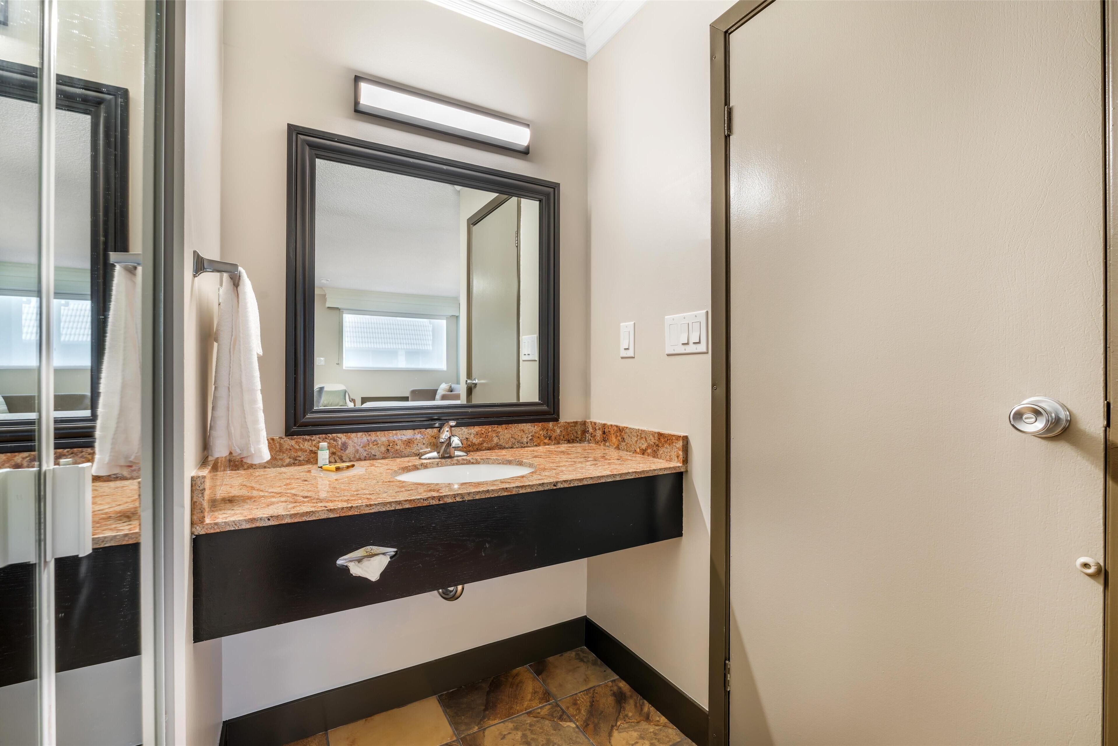 A bathroom with a black countertop, white sink, and a large mirror.