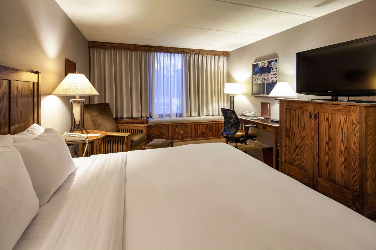 A hotel room with a large bed, a desk with a computer, a television, and a window with curtains.