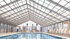 An indoor swimming pool with a high, glass ceiling and a view of the outside.
