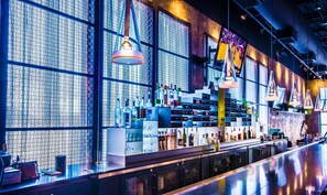 Un bar con pared estampada, estantes llenos de botellas e iluminación colgante.